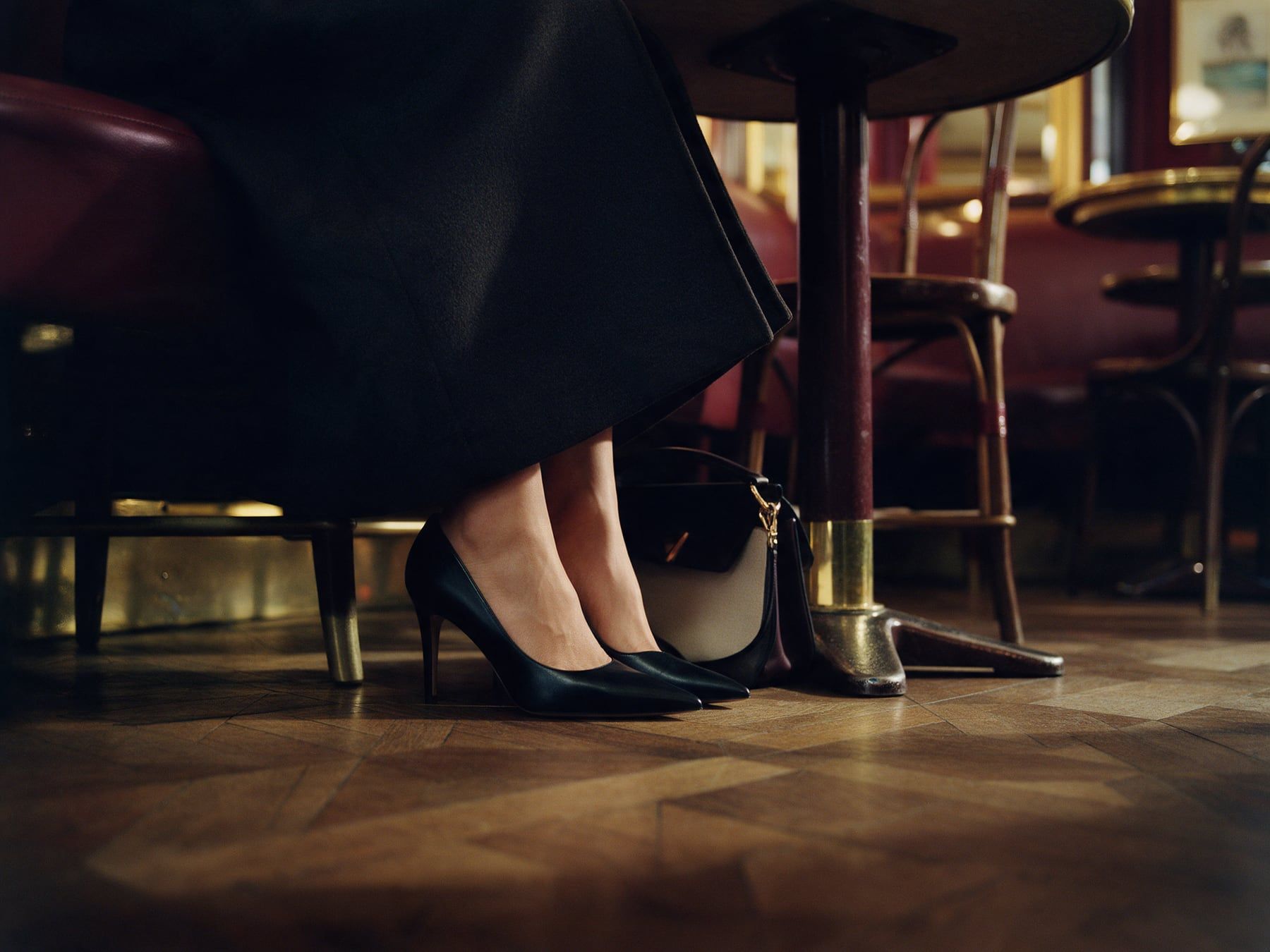Des escarpins noirs sous une table de café, l’ourlet d’un long manteau